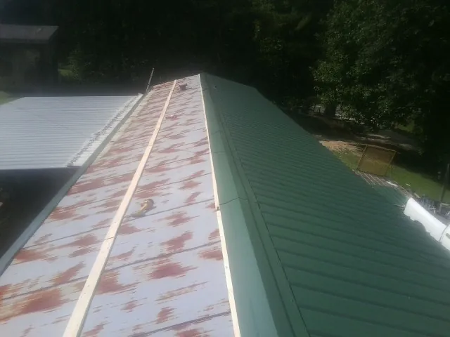 Old rusted panels beside newly installed green metal roofing — Wind Damage Roof Repair by Roofing Brothers in Dryden