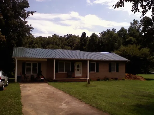 Dark green metal roof on a brick ranch with a covered porch in Dryden