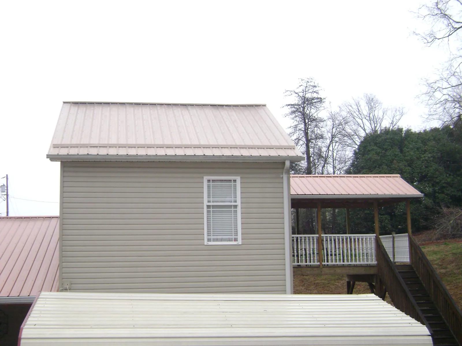 Tan metal roofs on a two story addition and attached porch, from a Roof Replacement job in Dryden